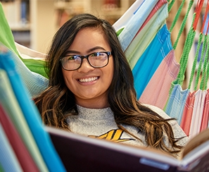 Female student reading book in colorful hammock in library