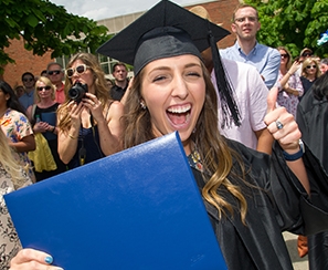 Happy female graduate with diploma in one hand and giving a thumbs up with her other hand