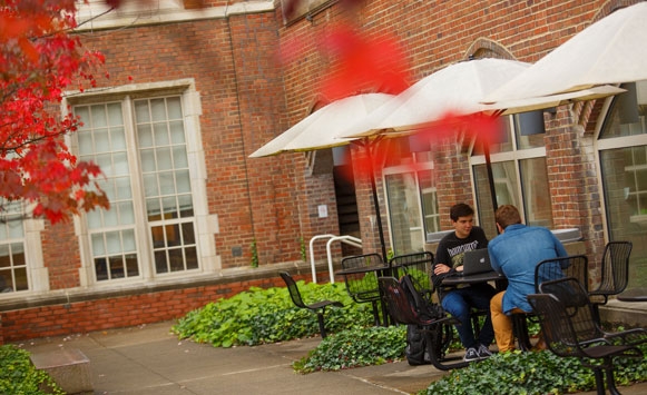 Two male students studying outside at a table in the courtyard in the fall