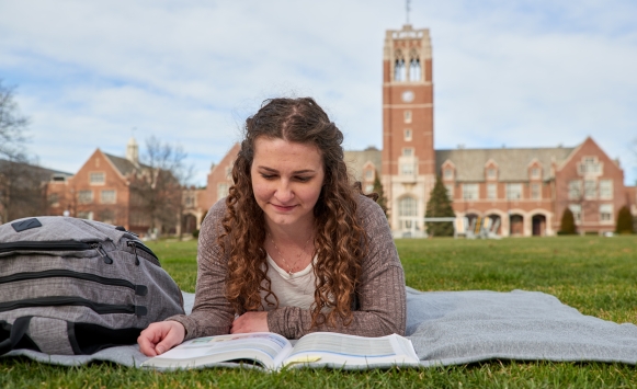 Female student studying on the quad with the Grasselli Clock Tower in the background