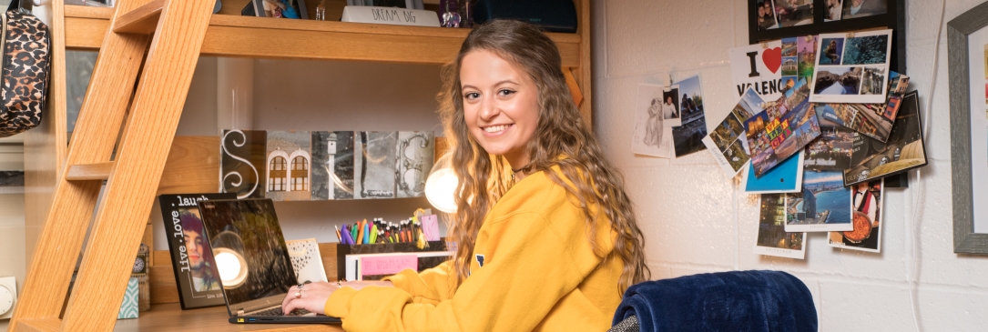 Student smiling and sitting at her desk in a residence hall room