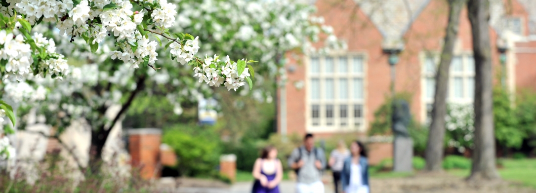 Group of students walking in front of the Administration Building with Rodman Hall in the background in the spring