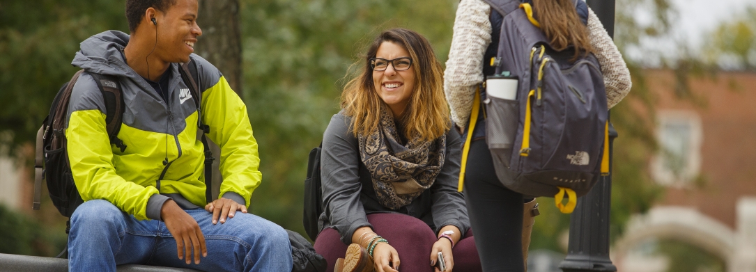 One male and two female students talking on a bench near the quad in the fall