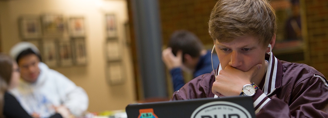 Male student on laptop in O'Malley Center with headphones in