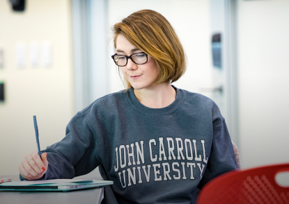 Female student wearing JCU sweatshirt sits in a classroom and writes. 