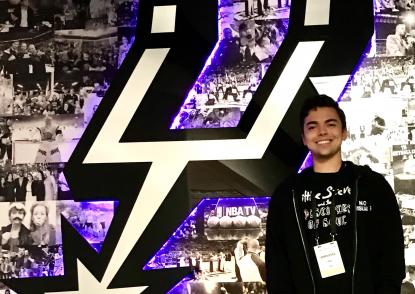 Brenan Betro stands in front of the San Antonio Spurs logo.