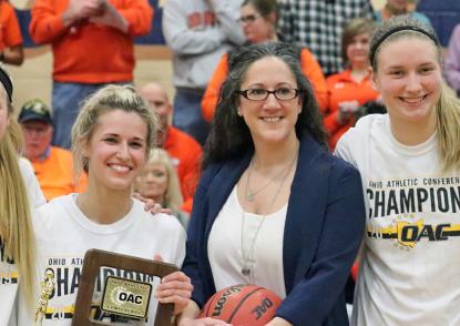 Kelly Morrone and her players pose together with a championship trophy and basketball. 