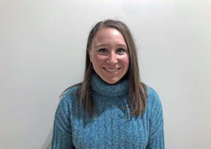 Megan Stechler stands in front of a white backdrop. Female wearing blue sweater