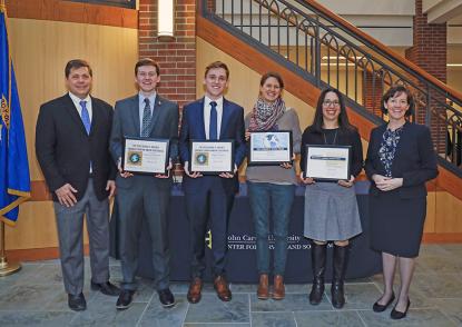 The four award winners stand between Dr. Ed Peck and Sr. Katherine Feely and hold up their awards.